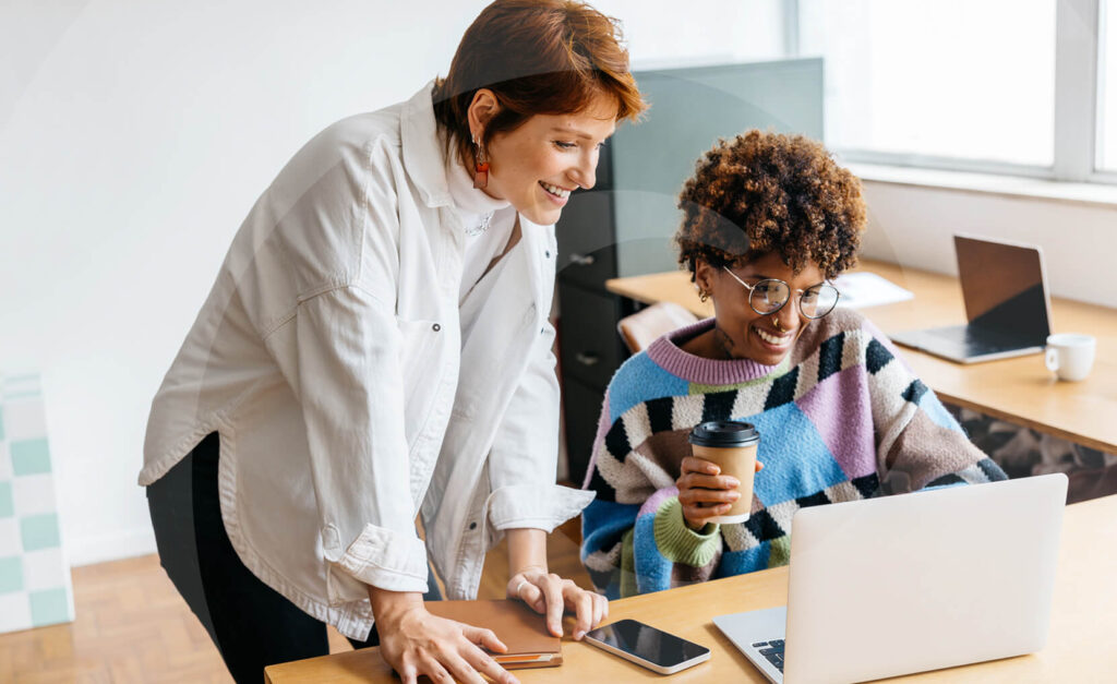 Two women smiling and looking at a laptop while they explore content trends for seo success.